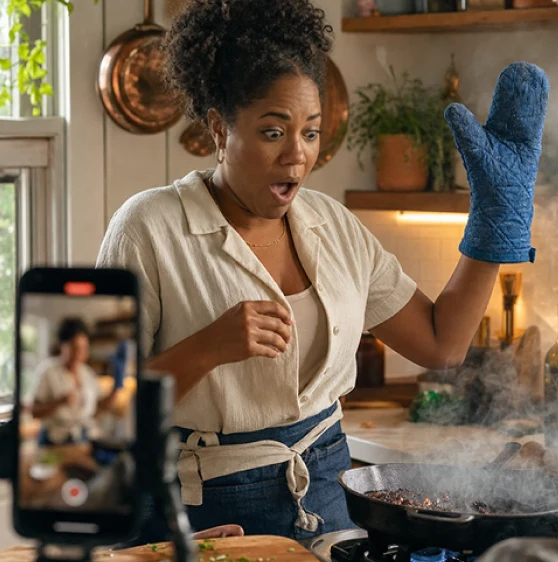A food creator reacting with surprise, cobalt oven mitt raised, while filming a cooking reel
